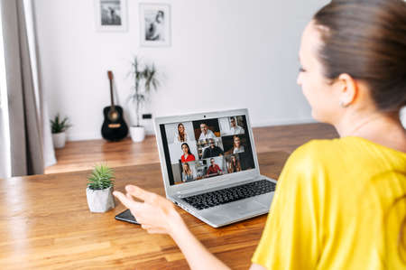 Virtual conference, online meeting. Young woman uses laptop app for communicating with several people friends or employees at same time together. Back view. Video call conceptの写真素材