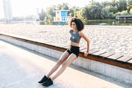 An athletic African-American young woman in sports outfit is doing morning exercises outdoor the city waterfrontの写真素材