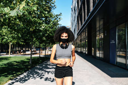 A biracial girl wearing a protective mask on the face with an afro hairstyle is running in the city...