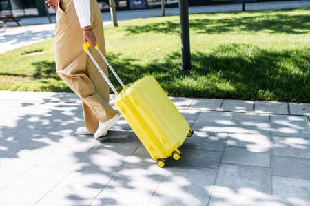 Female hands pull a yellow trolley bag outdoors. No faces visible. Travel timeの写真素材