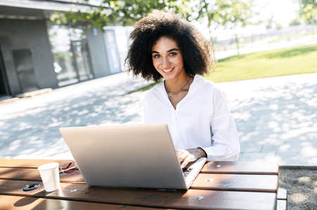 Attractive dark skinned woman using laptop computer for work, studying or watching videos outdoorsの写真素材