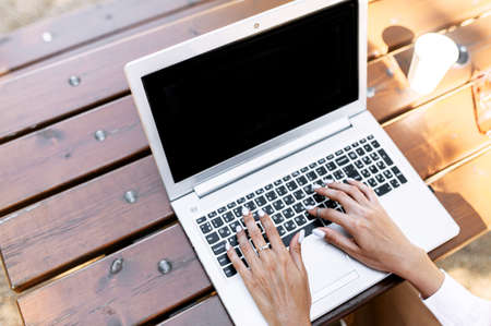 Female hands on a laptop keyboard outdoors. No faces visibleの写真素材
