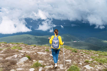 Recreation and trekking. Back view of a female hiker with sticks for nordic walks, a panoramic view on mountains on the backgroundの写真素材