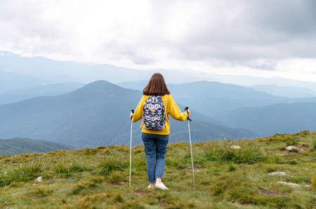 Young attractive woman with nordic walking poles hiking outdoors. Hiking and resting in mountains. Back view, full lengthの写真素材