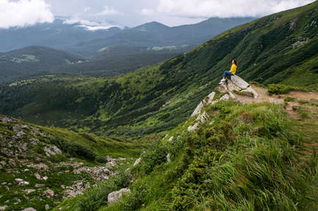 A woman sits on the top of the cliff and enjoying spectacular view on the mountains. Resting and recreation in the natureの写真素材