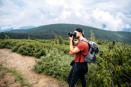 Male tourist hiking in a mountains. Side view of a guy with photo camera taking photo of a stunning landscapeの写真素材