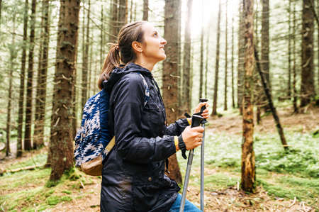 The woman with a backpack is engaged in scandinavian walking in a forest. Side viewの写真素材