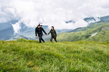 A couple in love walk holding hands on the top of mountain with a scenic view on the backgroundの写真素材