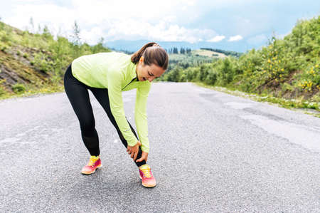 A young woman had a running injury with her legs while run outdoors. A suffering from pain woman holding ankleの写真素材