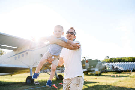 A dad and toddler spend time outdoors in an airplanes museum. A young father carries baby boy in...