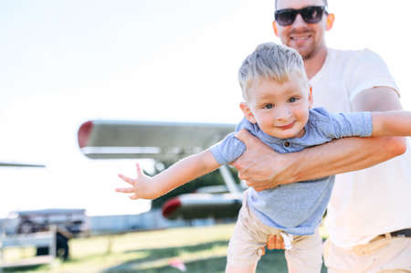 A cute little boy in hands of his dad outdoors. A toddler spread arms like an airplaneの写真素材