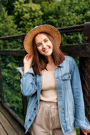 Young attractive woman in straw hat and casual jeans jacket outdoors. A brunette girl is looking at camera. Vertical portraitの写真素材