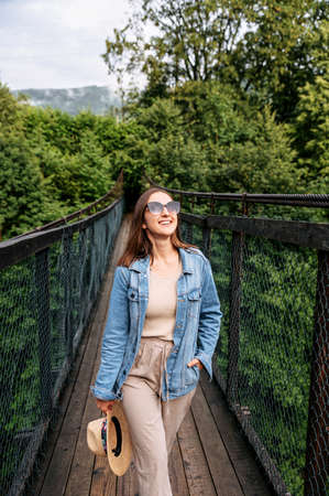 Young attractive woman is walking on suspension cable bridge among wild forest