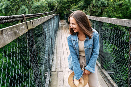 Young attractive woman stands on suspension cable bridge among wild forest and laughing happily. Good moodの写真素材
