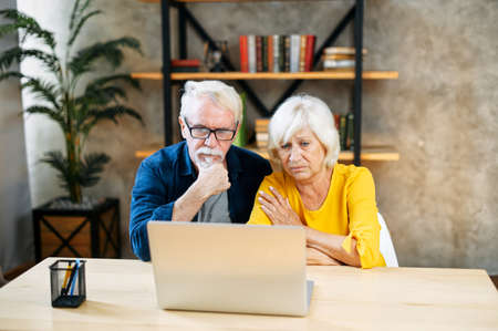 Sad senior couple looking at laptop screen and worrying about expenses at homeの写真素材