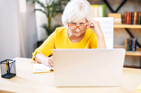 A senior concentrated business lady staring at the screen and lowered her eyeglasses while using laptopの写真素材