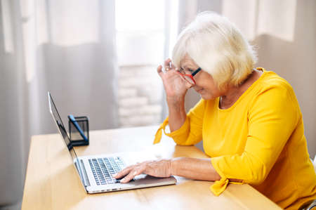 A senior concentrated business lady staring at the screen and lowered her eyeglasses while using laptop. Side viewの写真素材