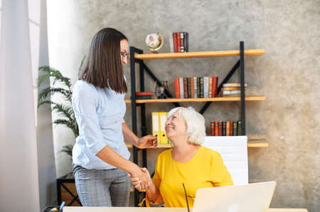 Friendly atmosphere in office. Two female colleagues diverse generation handshaking after successful...