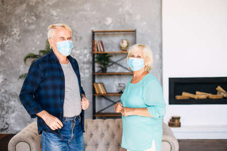 Joyful senior couple with a medical mask on their faces spends time together at home during pandemic, quarantineの写真素材