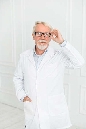 Vertical portrait of senior grey haired doctor in eyeglasses in clinic uniform, isolated on whiteの写真素材