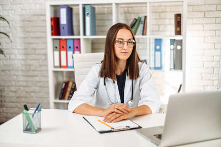 Female doctor with clipboard using laptop at office in the hospitalの写真素材
