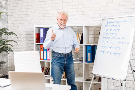 A senior male teacher with a whiteboard is streaming lessons, translating online classes during quarantine period. Distance studying conceptの写真素材