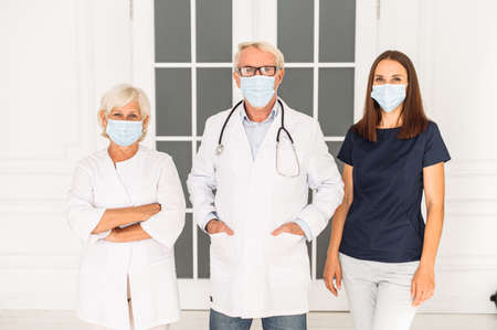 Team of doctors and nurse with a medical masks on the face looking at camera on the white background. A group of medical workers confronting the viral threatの写真素材
