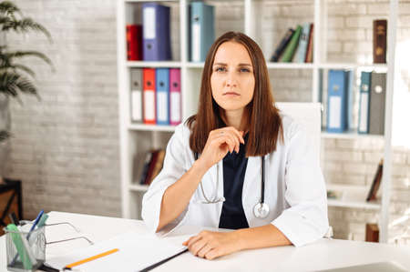 Webcam view of young puzzled female doctor in white wear with a stethoscope on the shoulders, she looks at camera and listens with a serious face. Online visit conceptの写真素材