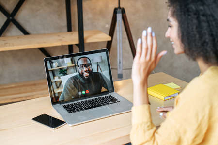 Back view african american woman talks via video with a black male colleague on the laptop screen. Virtual morning meeting, remote workの写真素材