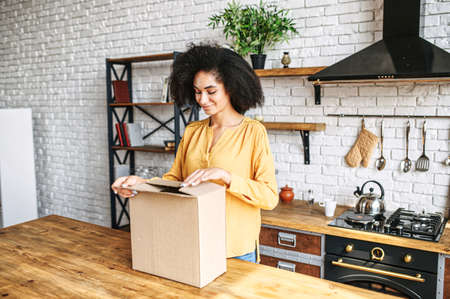 An african-american woman is unpacking parcel cardboard box with online orderの写真素材