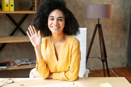 Video chat with attractive african american female colleague, she is greeting. Online meeting with a multi ethnic woman sitting at modern officeの写真素材