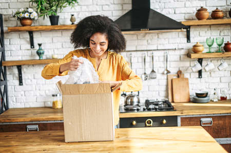 An african-american woman is unpacking parcel cardboard box with online orderの写真素材