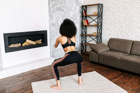 An african-american athletic woman is doing workout at home. Back view of female biracial millennial is doing sits up. Healthy lifestyle conceptの写真素材