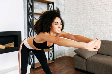 Attractive mixed-race woman in sportswear is warming up before workout at home.の写真素材