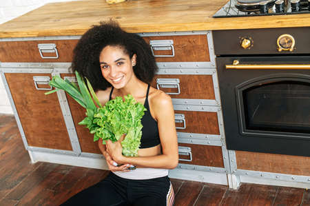 A cheerful african american woman in sportswear with an armful of fresh vegetablesの写真素材