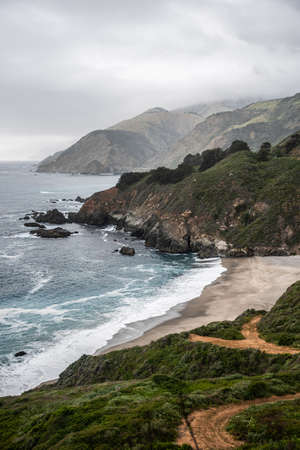 Panoramic ocean view in the cold and cloudy day, green hills and a sandy bay of California, USA. Vertical shotの写真素材
