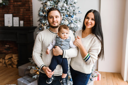 Loving parents and infant son near Christmas tree at home. New Year mood