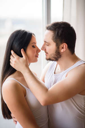 Tenderly portrait of couple in love at home. A bearded guy is touching hair of beautiful girlの写真素材
