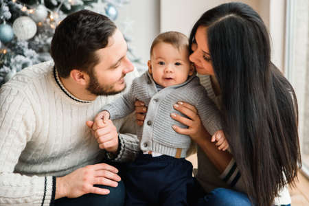 Happy family spends New Year holiday at home. A beautiful young mother and father are kissing cute...