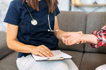 Nurse examining pulse rate of senior female patient at home appointment, faces are not visibleの写真素材