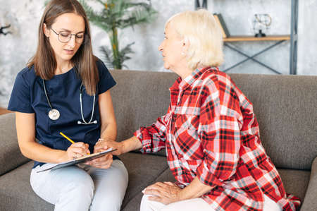 Senior woman and the young female doctor is talking during visit at homeの写真素材