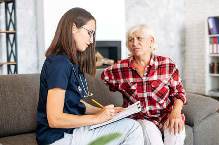 Senior woman and the young female doctor is talking during visit at homeの写真素材