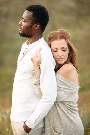 Multiracial couple in love in sunset light. A charming red haired woman with eyes closed hugging from the back an african-american manの写真素材