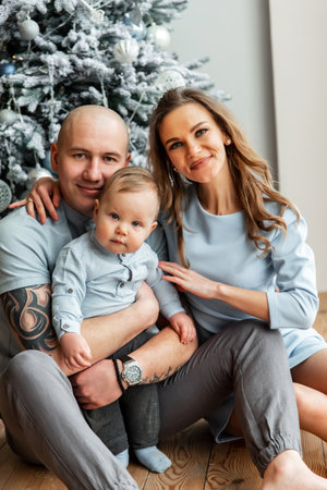 Christmas family portrait. A young family with a cute baby boy sit together on the floor near...