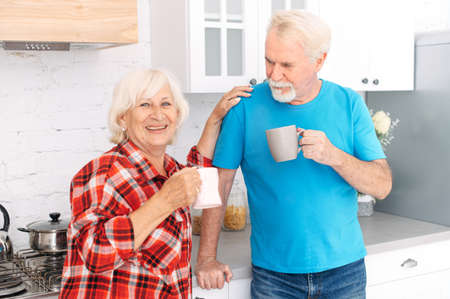 Senior couple is enjoying time together at home. Grandparents with cups of tea in the kitchenの写真素材