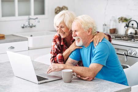 A couple of retired spouses use a laptop for leisure at home. Senior spouse enjoying spending time in networksの写真素材