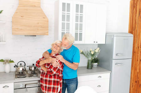 Cheerful senior couple in love is hugging in the kitchen at home. Love through the yearsの写真素材