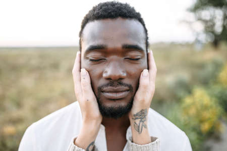Close-up picture of the face of handsome black guy, a white female palms are gently touching hisの写真素材