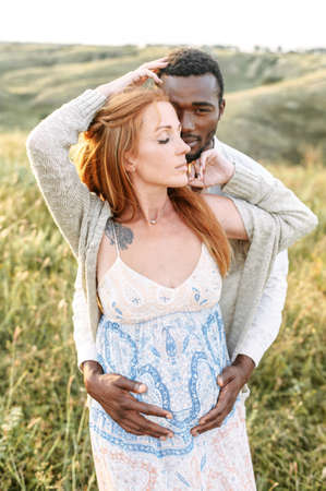 Multiracial spouses are looking forward for a baby. A pregnant wife dreams with eyes closed, her husband touching tummy tenderlyの写真素材