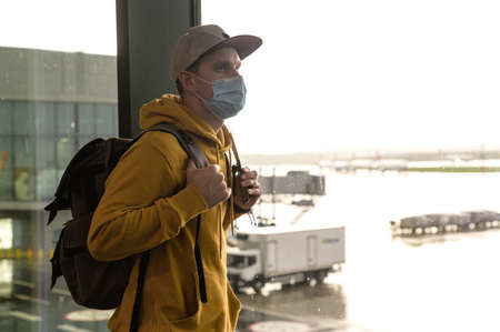 Travels during pandemic. A young man wearing surgical mask with is waiting for boarding in airport